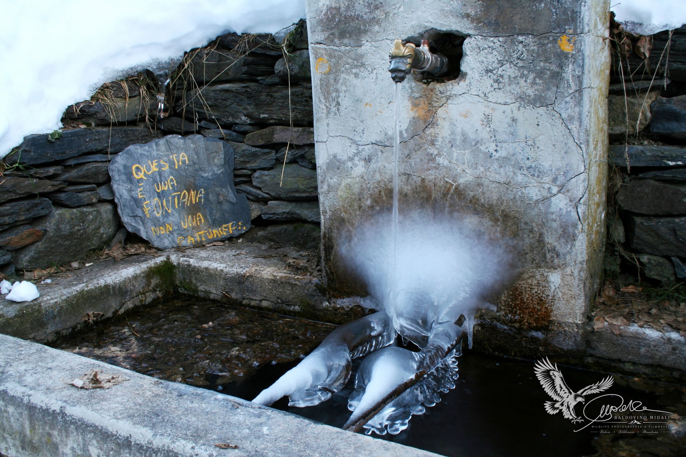 Antica fontana in pietra con acqua e ghiaccio in un ambiente innevato
